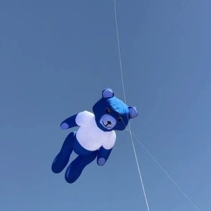 A blue inflatable teddy bear kite flying high in a blue sky.