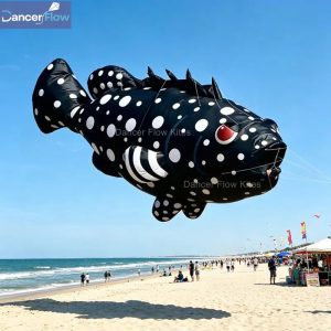 A black inflatable fish kite with white spots, large eyes and spiky fins.