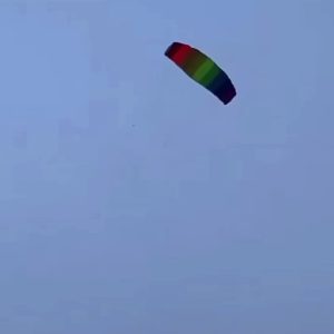 A small rainbow parafoil kite flying high against a blue sky.