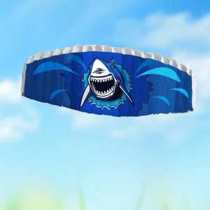 A blue parafoil kite with a smiling shark graphic flying against the sky.